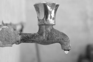 %Title% | Pf Plumbing A close-up of an old, weathered metal water tap with a single droplet of water hanging from the spout.